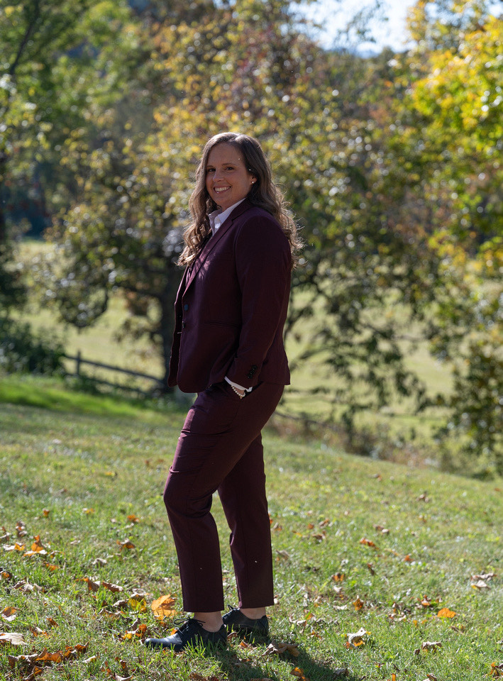 A woman standing in a maroon wedding suit. 